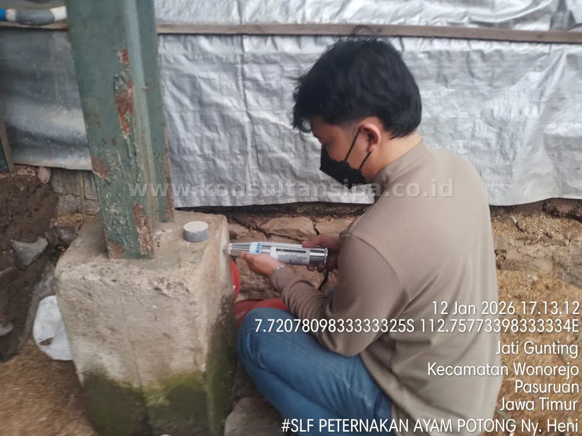 Teknisi melakukan uji hammer test pada struktur beton kolom bangunan peternakan untuk SLF di Pasuruan
